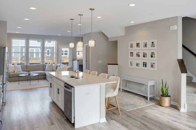 kitchen with light wood-style flooring, a sink, open floor plan, a kitchen breakfast bar, and stainless steel dishwasher