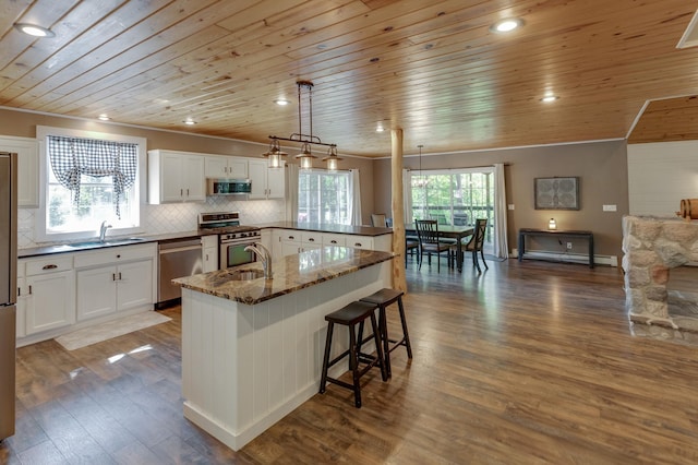 kitchen featuring stainless steel appliances, wood ceiling, a sink, a breakfast bar, and white cabinetry
