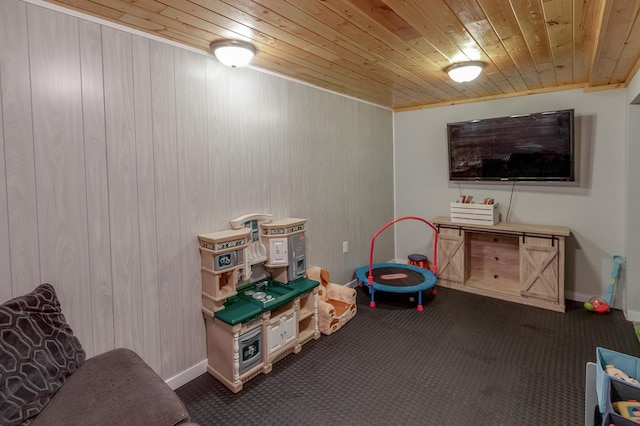 playroom with wood ceiling, dark colored carpet, baseboards, and wood walls