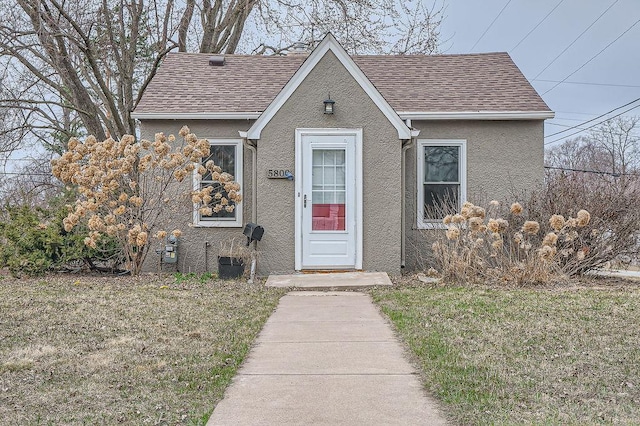 view of front of house featuring a front lawn, a shingled roof, and stucco siding