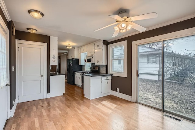 kitchen featuring white microwave, visible vents, gas range, dark countertops, and black fridge with ice dispenser