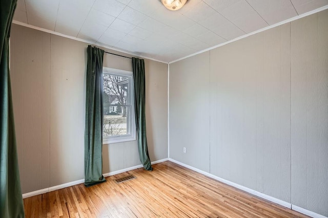spare room with crown molding, wood finished floors, baseboards, and visible vents