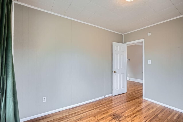 empty room with crown molding, baseboards, and light wood-style floors