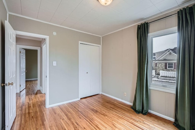 unfurnished bedroom featuring a closet, light wood-style flooring, baseboards, and ornamental molding