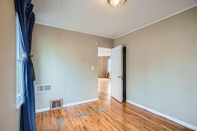 unfurnished room featuring visible vents, baseboards, ornamental molding, and light wood-style flooring