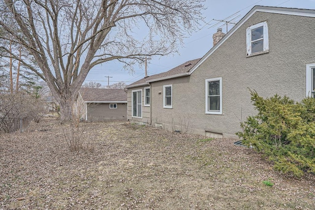 exterior space featuring an outbuilding, stucco siding, and a chimney