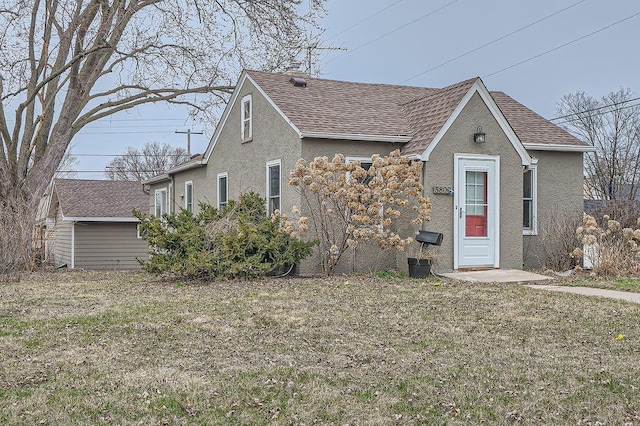 view of front of home with a front yard, a shingled roof, and stucco siding