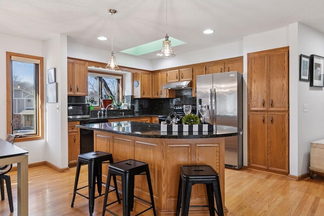 1001 Gramsey Pl, Burnsville, MN 55306 - kitchen featuring stainless steel appliances, under cabinet range hood, backsplash, brown cabinetry, and light wood-style flooring
