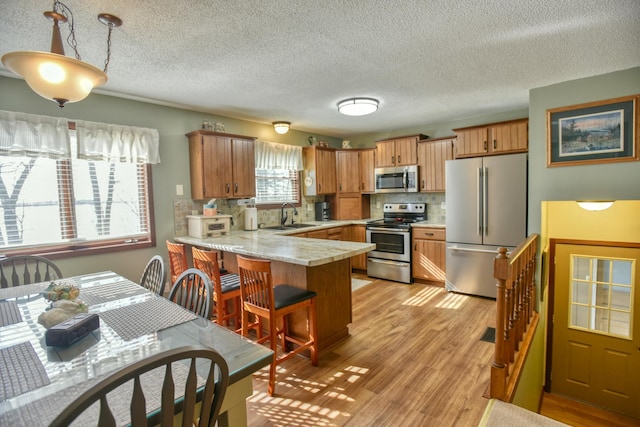 kitchen with a peninsula, light countertops, tasteful backsplash, a sink, and appliances with stainless steel finishes