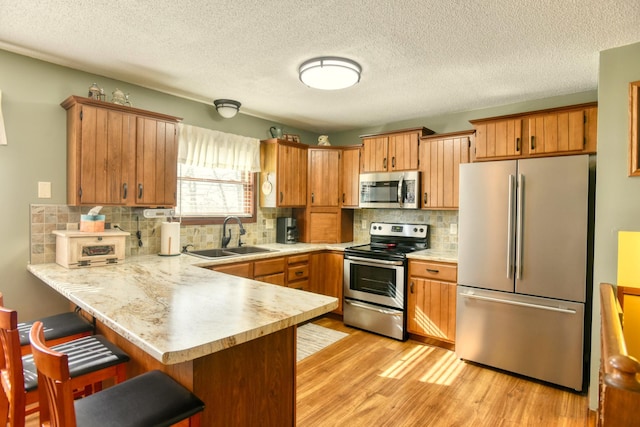 kitchen with a peninsula, light countertops, a sink, light wood-style flooring, and appliances with stainless steel finishes