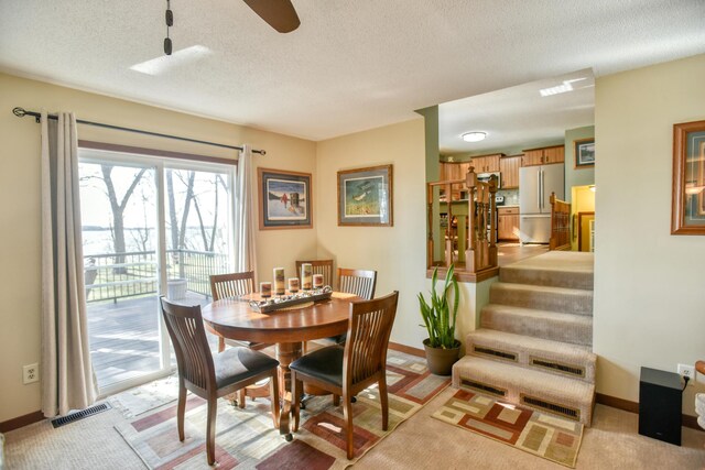 dining room featuring a textured ceiling, light colored carpet, visible vents, baseboards, and stairs