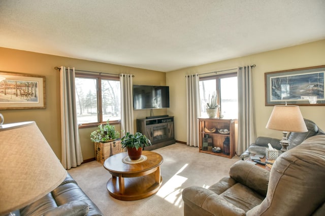 living room featuring a healthy amount of sunlight, light carpet, a glass covered fireplace, and a textured ceiling