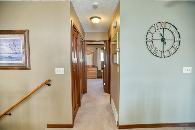 corridor featuring baseboards, a textured ceiling, light carpet, and an upstairs landing