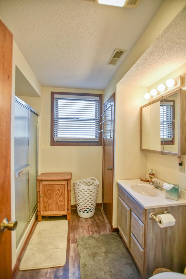 full bath with vanity, a textured ceiling, visible vents, and a stall shower