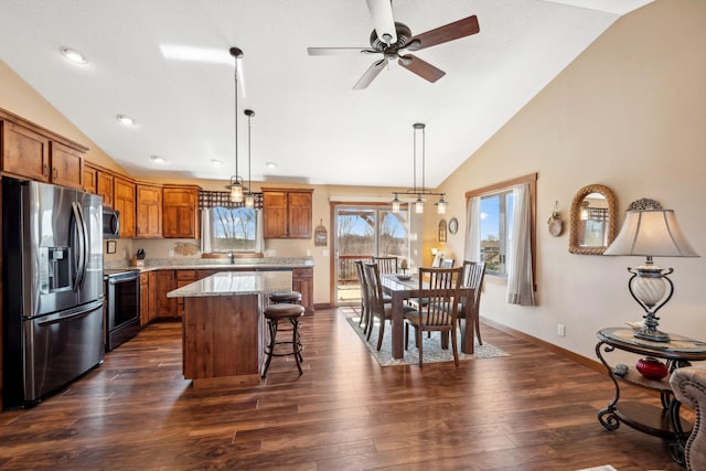 kitchen featuring a breakfast bar, brown cabinets, stainless steel appliances, a kitchen island, and lofted ceiling