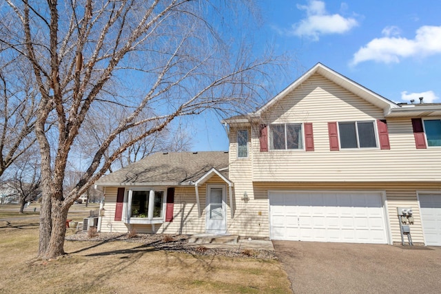 split level home with an attached garage, driveway, and central AC unit