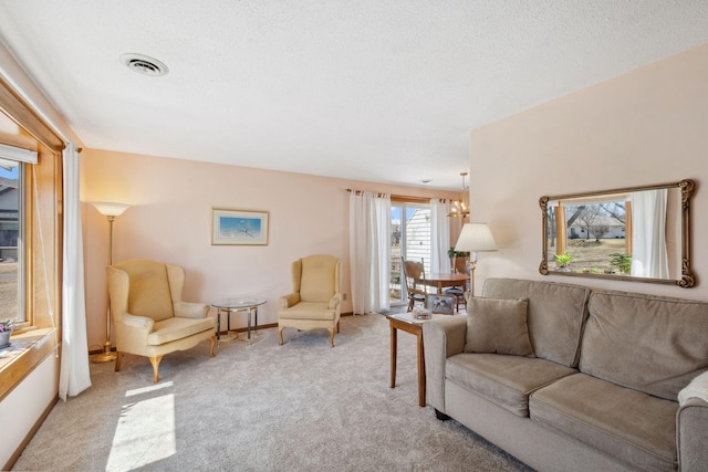 living area with visible vents, baseboards, an inviting chandelier, a textured ceiling, and light colored carpet