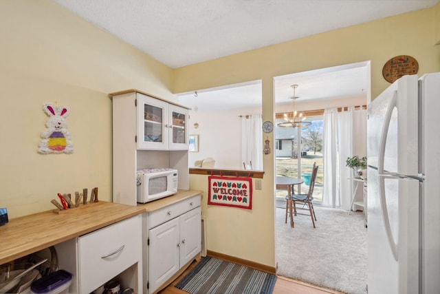 kitchen with glass insert cabinets, white cabinets, a notable chandelier, white appliances, and carpet floors