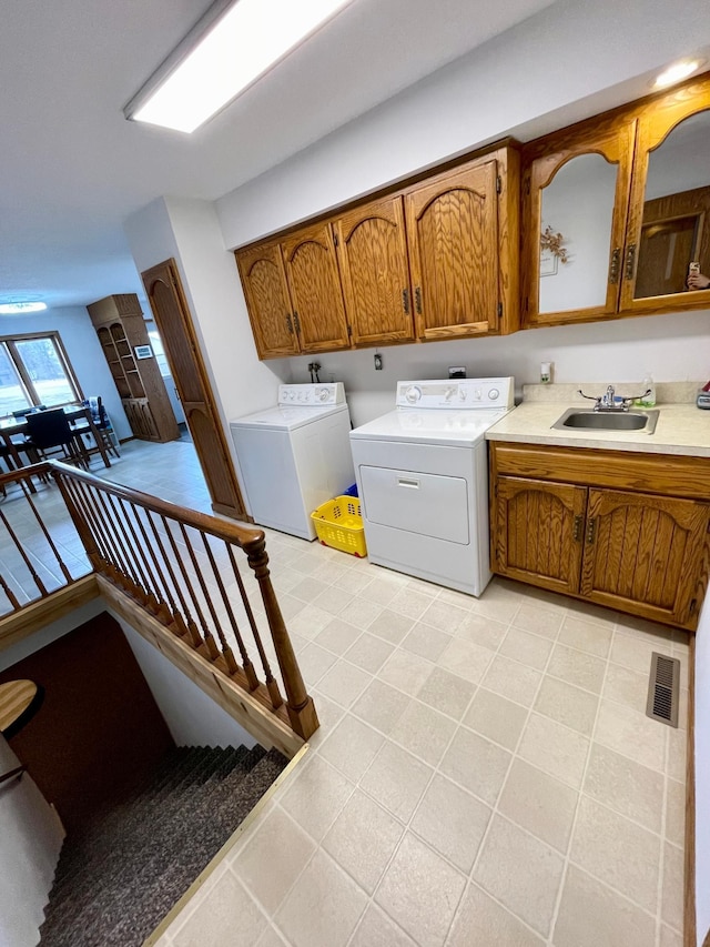 clothes washing area featuring light tile patterned floors, visible vents, washing machine and clothes dryer, a sink, and cabinet space