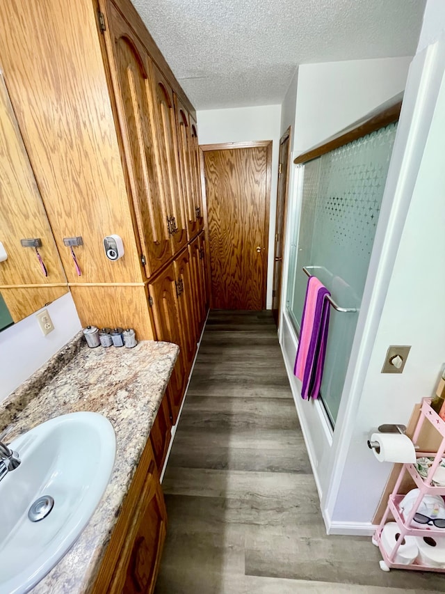 full bathroom with vanity, a textured ceiling, a stall shower, and wood finished floors