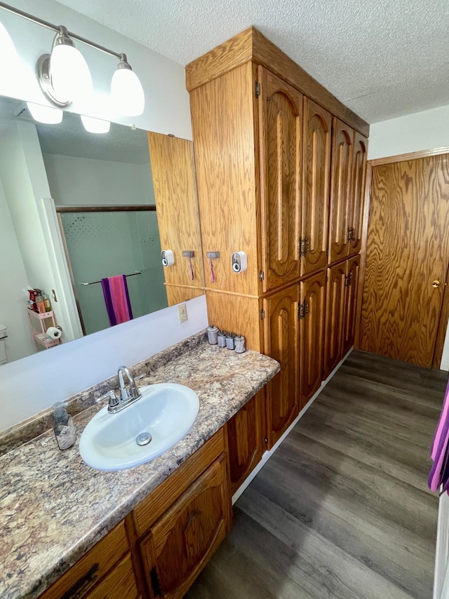 full bath with vanity, a textured ceiling, a stall shower, and wood finished floors