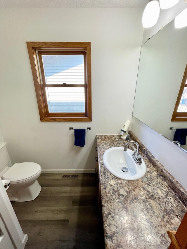 bathroom with visible vents, baseboards, toilet, vanity, and wood finished floors