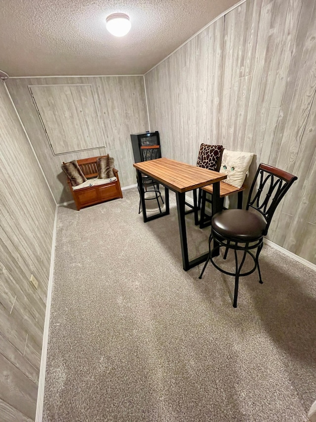 carpeted dining area featuring a textured ceiling and wood walls