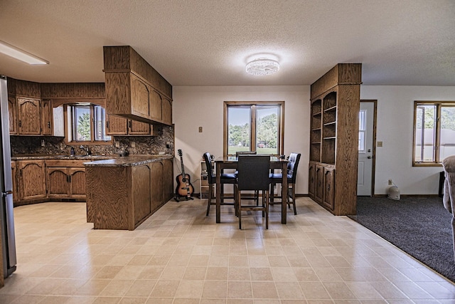 123 3rd St, Bluffton, MN 56518 - kitchen with a peninsula, dark countertops, a textured ceiling, backsplash, and brown cabinets