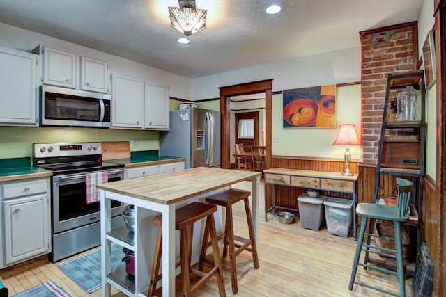 kitchen with a textured ceiling, wainscoting, butcher block countertops, appliances with stainless steel finishes, and wooden walls