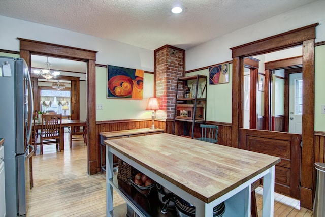 dining room featuring a textured ceiling, light wood finished floors, wooden walls, an inviting chandelier, and wainscoting