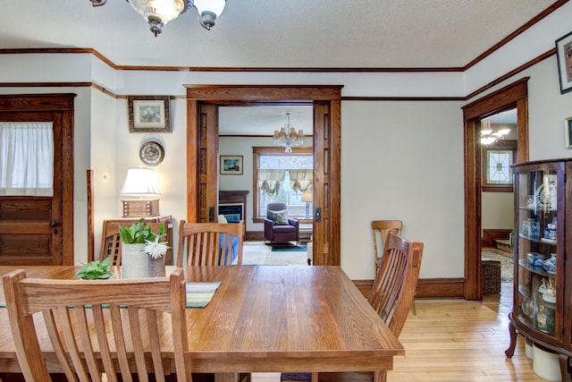 dining space featuring a chandelier, ornamental molding, a textured ceiling, and light wood-type flooring