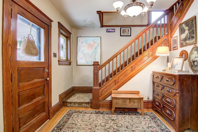 foyer with baseboards, stairway, an inviting chandelier, and light wood-style floors