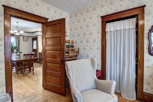 living area featuring an inviting chandelier, ornamental molding, hardwood / wood-style floors, and wallpapered walls