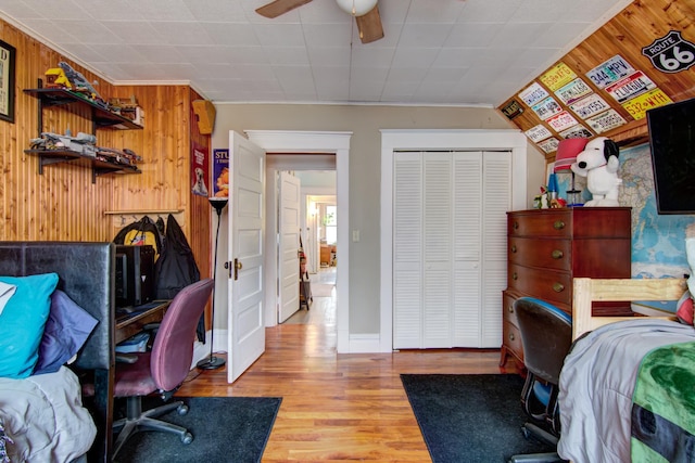 bedroom with a closet, baseboards, ceiling fan, wood walls, and wood finished floors