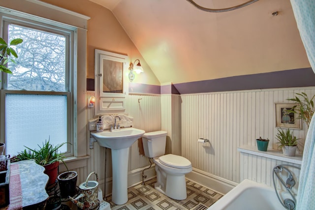 bathroom with toilet, wainscoting, a tub to relax in, a sink, and vaulted ceiling