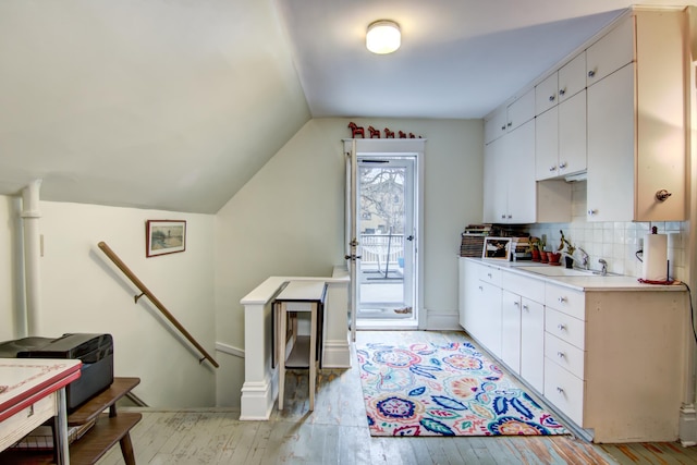 kitchen with a sink, light wood-type flooring, light countertops, decorative backsplash, and lofted ceiling