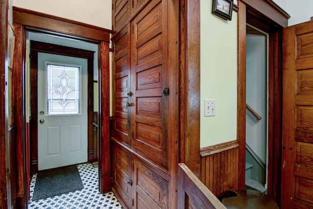 doorway to outside with tile patterned floors, wooden walls, and wainscoting