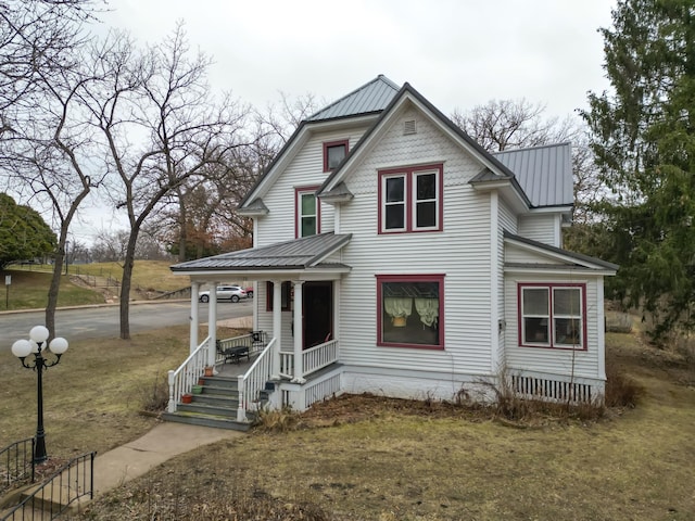 victorian house featuring metal roof, a porch, and a front lawn