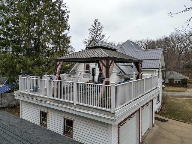 back of house featuring a garage, metal roof, concrete driveway, a gazebo, and a balcony
