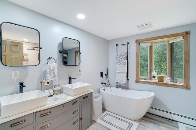 108 1st St, Kenyon, MN 55946 - bathroom with baseboard heating, double vanity, a freestanding bath, wood finished floors, and recessed lighting