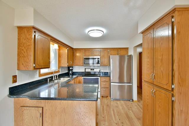 kitchen with light wood-type flooring, a peninsula, brown cabinets, stainless steel appliances, and a sink