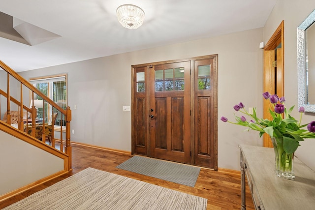 entryway featuring baseboards, stairs, light wood finished floors, and a chandelier