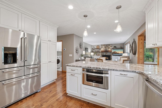 kitchen with appliances with stainless steel finishes, light wood finished floors, washer / dryer, recessed lighting, and white cabinetry