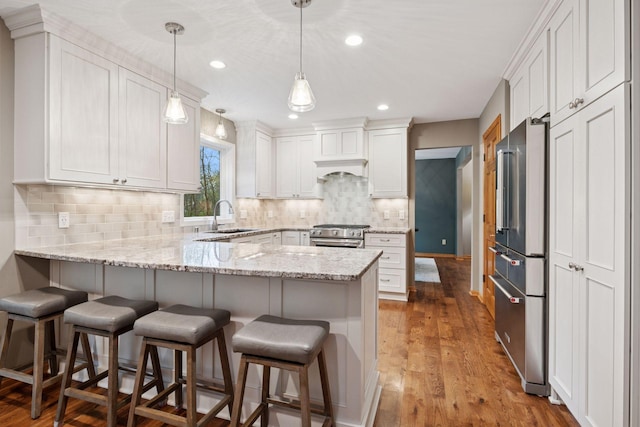 kitchen featuring a peninsula, white cabinets, light stone counters, a sink, and premium appliances