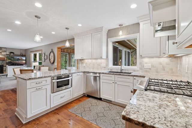 kitchen with appliances with stainless steel finishes, hanging light fixtures, a sink, a peninsula, and backsplash
