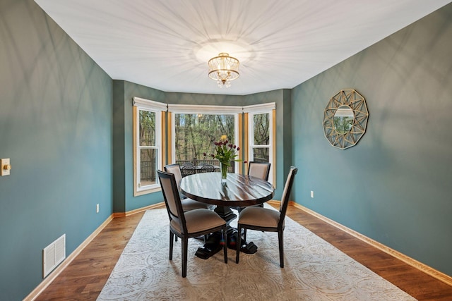 dining space featuring visible vents, baseboards, wood finished floors, and a chandelier