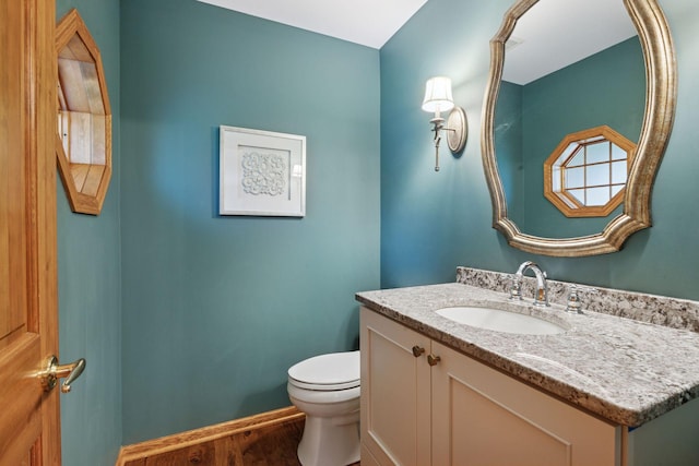 half bathroom with vanity, baseboards, wood finished floors, and toilet