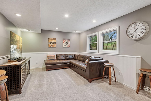 living area featuring carpet flooring, a textured ceiling, and a wainscoted wall
