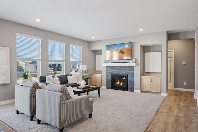 living room with recessed lighting, hardwood / wood-style floors, a stone fireplace, and baseboards