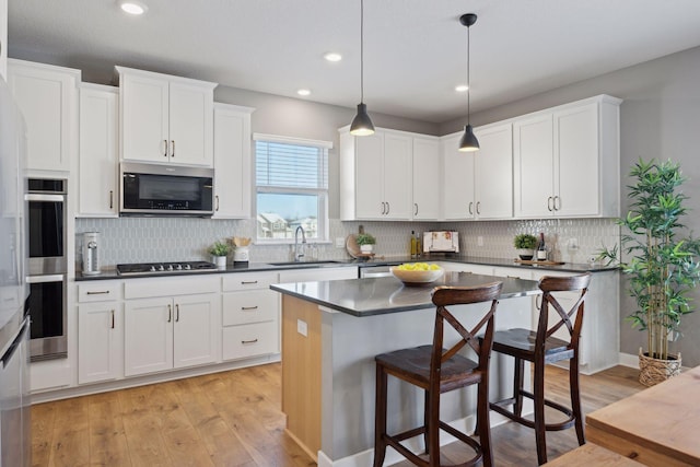 kitchen with light wood-style floors, appliances with stainless steel finishes, a sink, dark countertops, and a breakfast bar area